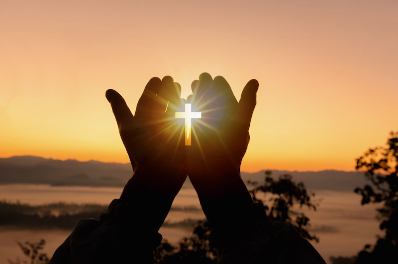 hand open in worship palm up with cross at sunset